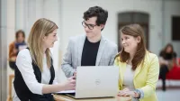 Cross-Border e-Commerce | Studia podyplomowe w Opolu | Uniwersytet WSB Merito Opole: Główna grafika: Opole - studia podyplomowe -Cross-Border e-Commerce- uczestnicy studiów podyplomowych rozmawiają miedzy sobą na korytarzu z otwartym laptopem na stoliku