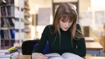 Pedagogika | Studia II stopnia w Opolu | Uniwersytet WSB Merito Opole: Kobieta w ciemnym swetrze czyta książkę w bibliotece