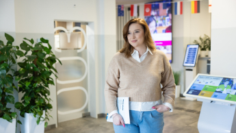 Seksuologia | Studia podyplomowe w Opolu | Uniwersytet WSB Merito Opole: Główna grafika: Opole - studia podyplomowe - Seksuologia - Kobieta trzymająca w dłoni książkę, stoi na korytarzu