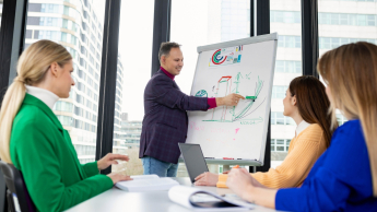 Zarządzanie jakością w branży automotive | Studia podyplomowe w Opolu | Uniwersytet WSB Merito Opole: Główna grafika: Opole - studia podyplomowe - Zarządzanie jakością w branży automotive - grupa osób słuchająca wypowiedzi mężczyzny stojącego przy tablicy