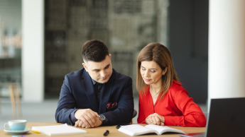 Główna grafika: Opole - studia podyplomowe - E-commerce i zarządzanie platformami sprzedażowymi- uczestnicy studiów podyplomowych siedzą przy biurku i analizują treści z notatnika