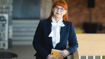 HR menedżer | Studia podyplomowe w Opolu | Uniwersytet WSB Merito Opole: Główna grafika: Opole - studia podyplomowe -HR menedżer- uczestniczka studiów podyplomowych opiera się o balustradę trzymając w ręce książkę