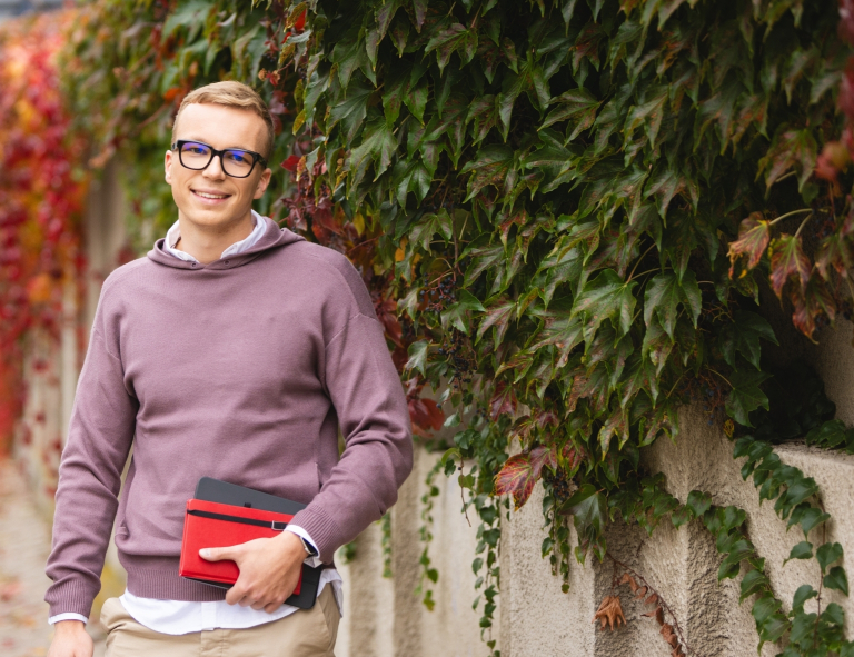 Zarządzanie | Studia II stopnia ze studiami podyplomowymi w Opolu | Uniwersytet WSB Merito Opole: Student stojący na zewnątrz, trzyma książki