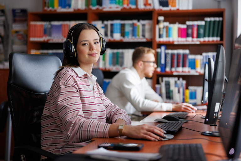 Nasz budynek | Uniwersytet WSB Merito Opole: Studentka w bibliotece, korzysta z słuchawek wyciszających