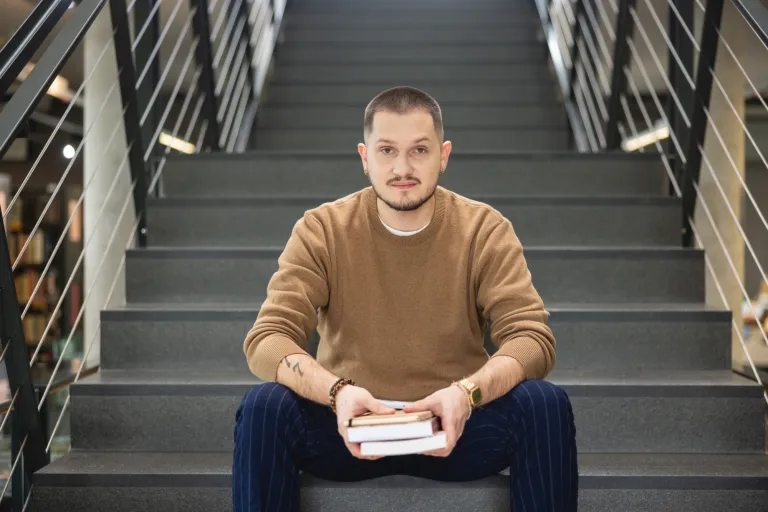 Zarządzanie | Studia II stopnia ze studiami podyplomowymi w Opolu | Uniwersytet WSB Merito Opole: Student siedzący na schodach biblioteki, trzyma książki