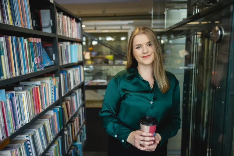 Pedagogika resocjalizacyjna z socjoterapią | Studia II stopnia ze studiami podyplomowymi  | Uniwersytet WSB Merito Opole: Studentka stojąca między regałami w bibliotece