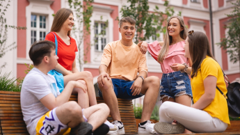 Outsourcing rozwiązań chmurowych | Studia II stopnia w Poznaniu | Uniwersytet WSB Merito w Poznaniu: 5 studentów siedzi na ławce w centrum miasta i rozmawiają w wesołej atmosferze