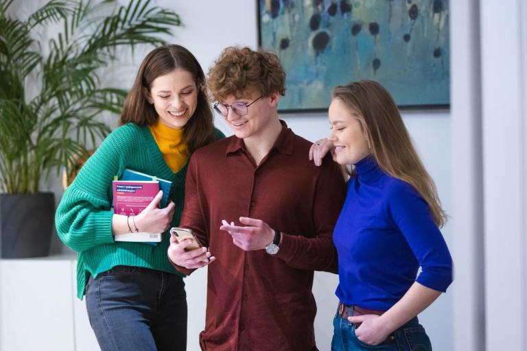 Organizacje i koła naukowe | Uniwersytet WSB Merito w Poznaniu: Troje studentów z uśmiechem przegląda telefon.