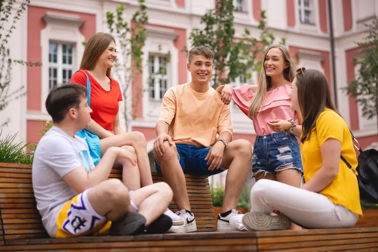 Psychologia w biznesie | Studia II stopnia w Poznaniu | Uniwersytet WSB Merito w Poznaniu: 5 studentów siedzi na ławce w centrum miasta i rozmawiają w wesołej atmosferze