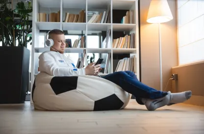 Poradniki - dzielimy się wiedzą | Uniwersytet WSB Merito: Chłopak siedzący na pufie w słuchawkach i z telefonem w dłoni