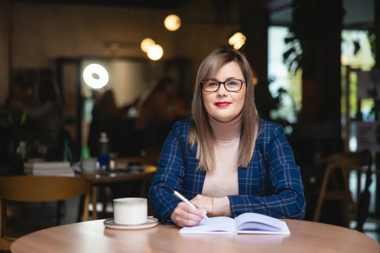 Jak zmienia się marketing wraz z pokoleniami klientów? | Blog "okiem praktyków" | Uniwersytet WSB Merito: Kobieta elegancko ubrana siedząca przy stole.