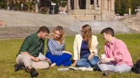 Psychologia społeczna | Studia jednolite magisterskie w Szczecinie | Uniwersytet WSB Merito Szczecin: Grupa studentów siedzi na trawie i wspólnie uczy się z książek w plenerze.