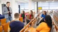 Zarządzanie bezpieczeństwem i higiena pracy | Studia podyplomowe w Szczecinie | Uniwersytet WSB Merito Szczecin: Wykładowca rozmawia ze studentami w auli, prowadząc swobodne zajęcia w małej grupie.
