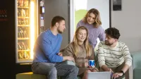 Zarządzanie kryzysowe | Studia I stopnia w Szczecinie | Uniwersytet WSB Merito Szczecin: Czwórka młodych osób siedzi razem w strefie relaksu, rozmawiając i pracując przy laptopie.