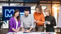 E-commerce Academy | Studia podyplomowe w Szczecinie | Uniwersytet WSB Merito Szczecin: Grupa czterech osób pracuje wspólnie przy stole w nowoczesnym biurze.
