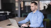 Digital Marketing Masterclass | Studia podyplomowe w Szczecinie | Uniwersytet WSB Merito Szczecin: Mężczyzna pracuje przy laptopie w nowoczesnej sali konferencyjnej, skupiony na ekranie.