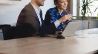 Zarządzanie przedsiębiorstwem | Studia I stopnia w Szczecinie | Uniwersytet WSB Merito Szczecin: Dwie osoby siedzą przy stole w sali konferencyjnej, pracując wspólnie przy laptopie.
