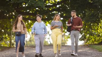 Administracja i bezpieczeństwo wewnętrzne | Studia II stopnia w Szczecinie | Uniwersytet WSB Merito Szczecin: Czworo studentów spaceruje alejką w parku, rozmawiając i uśmiechając się.