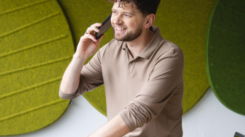 Audyt wewnętrzny | Studia podyplomowe w Szczecinie | Uniwersytet WSB Merito Szczecin: Student rozmawia przez telefon w nowoczesnej przestrzeni uczelni, z laptopem i notatkami na biurku.