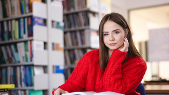 Pedagogika opiekuńczo-wychowawcza i resocjalizacja | Studia I stopnia w Szczecinie | Uniwersytet WSB Merito Szczecin: Studentka siedzi w bibliotece, czytając książkę.
