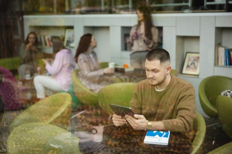 Cyfrowy uniwersytet | Uniwersytet WSB Merito Szczecin: Student Uniwersytetu WSB Merito korzystający z tabletu i pijący kawę na fotelu w strefie relaksu