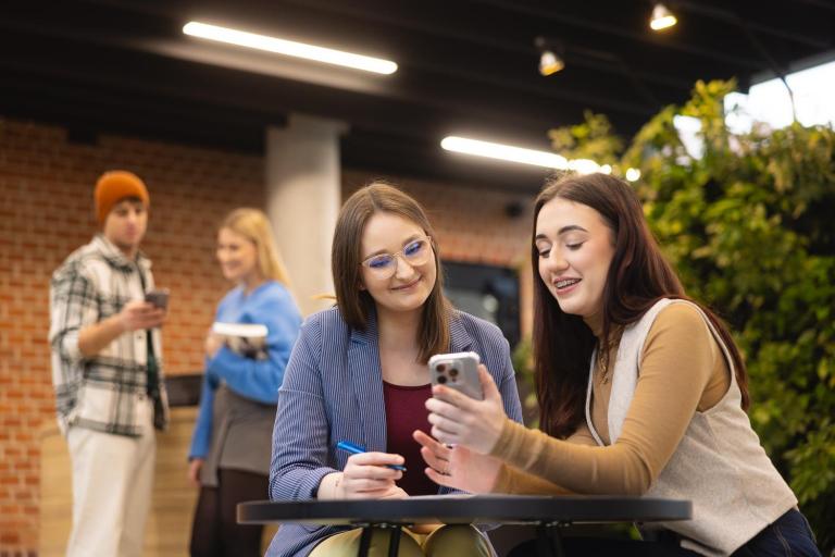 Maturzyści | Uniwersytet WSB Merito Szczecin: Studentka Uniwersytetu WSB Merito pokazuje ekran telefonu innej studentce