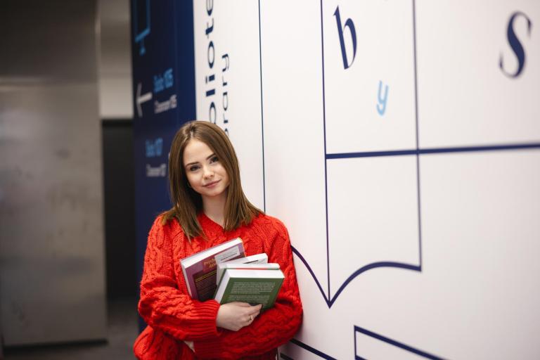 Pedagogika przedszkolna i wczesnoszkolna | Studia jednolite magisterskie w Szczecinie | Uniwersytet WSB Merito Szczecin: Studentka z książkami przy bibliotece, gotowa do nauki