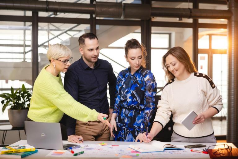 Zarządzanie i marketing | Studia II stopnia w Szczecinie | Uniwersytet WSB Merito Szczecin: Pięć osób pracuje kreatywnie przy stole, analizując notatki i rysunki.