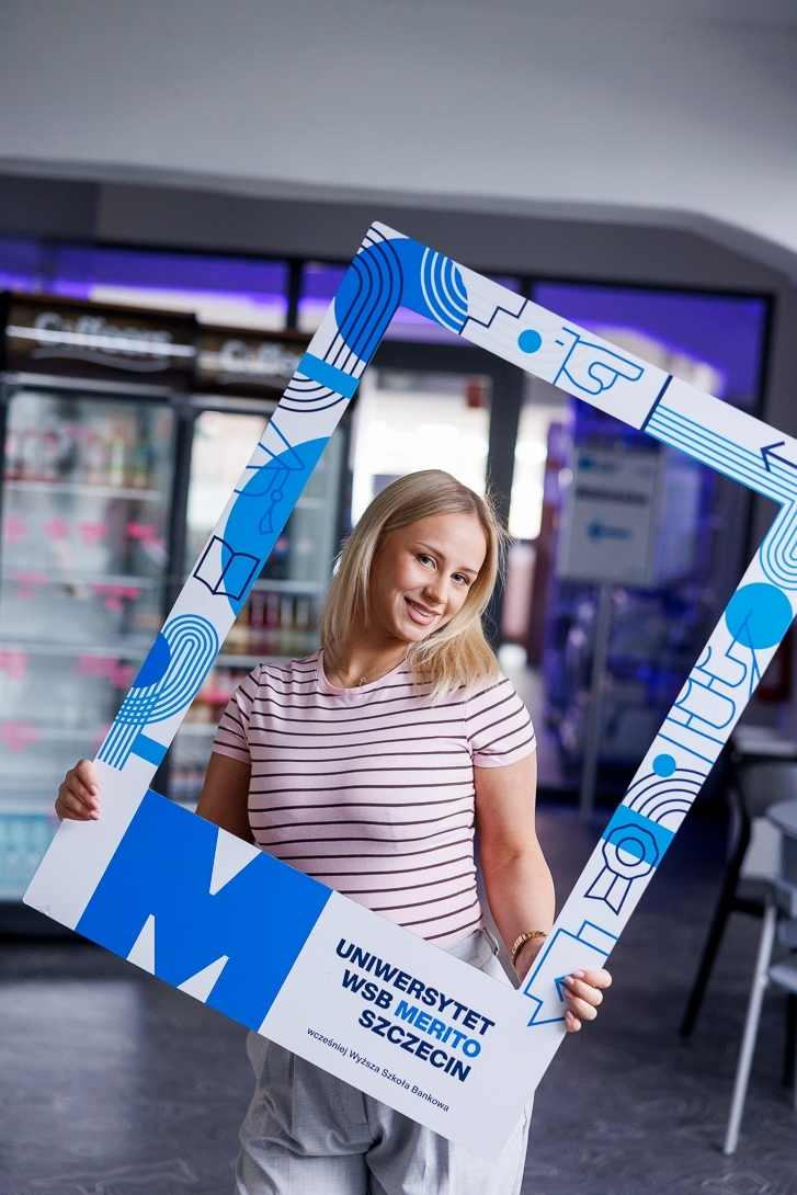Ekokosmetyka | Studia I stopnia w Szczecinie | Uniwersytet WSB Merito Szczecin: Dziewczyna pozuje z dużą ramką uczelni.