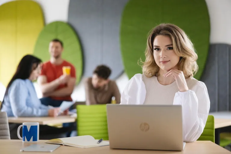 Zarządzanie | Studia II stopnia w Szczecinie | Uniwersytet WSB Merito Szczecin: Studentka pracuje przy laptopie w nowoczesnej strefie wspólnej, w tle inni studenci.