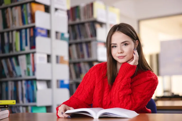 Odnowa biologiczna i wellness | Studia I stopnia w Szczecinie | Uniwersytet WSB Merito Szczecin: Studentka siedzi w bibliotece, czytając książkę.