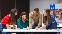 Poznaj nas | Uniwersytet WSB Merito w Toruniu: grupa uśmiechniętych studentów pracująca nad projektem przy stole