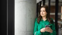 Menedżer przedsiębiorstwa turystycznego | Studia II stopnia w Toruniu | Uniwersytet WSB Merito w Toruniu: Główna grafika: Toruń - studia licencjackie - Studentka w zielonej koszuli pozująca do zdjęcia na korytarzu