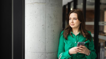 Menedżer przedsiębiorstwa turystycznego | Studia II stopnia w Toruniu | Uniwersytet WSB Merito w Toruniu: Główna grafika: Toruń - studia licencjackie - Studentka w zielonej koszuli pozująca do zdjęcia na korytarzu