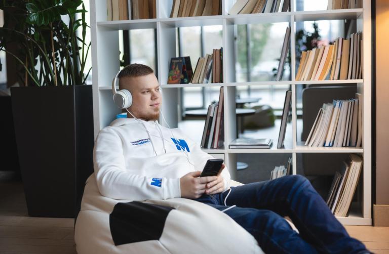 Cyfrowy uniwersytet | Uniwersytet WSB Merito w Toruniu: student ze słuchawkami na uszach i telefonem w ręku siedzi na pufie