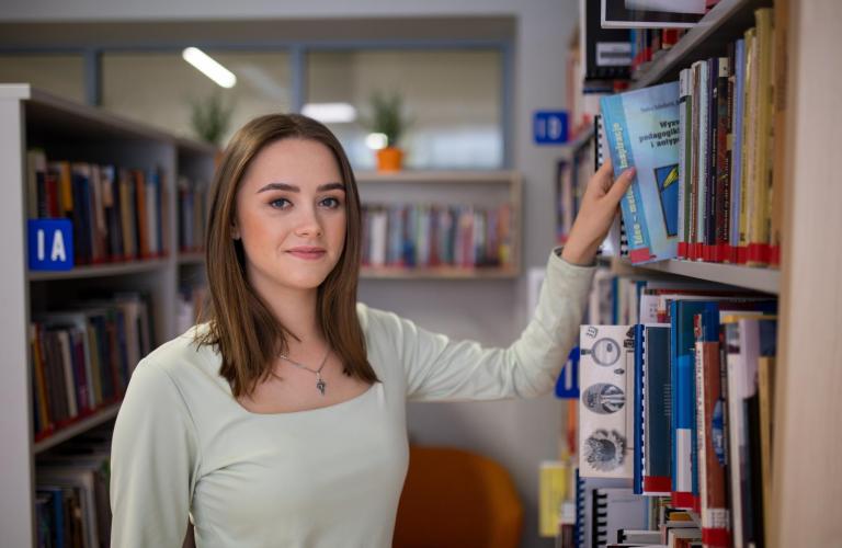 Wyniki wyszukiwania | Uniwersytet WSB Merito w Toruniu: studentka w bibliotece przy regale z książkami
