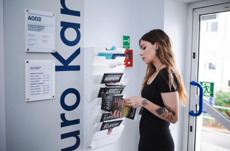 Biuro Karier | Uniwersytet WSB Merito w Toruniu: studentka przed gabinetem biura karier, przegląda magazyn