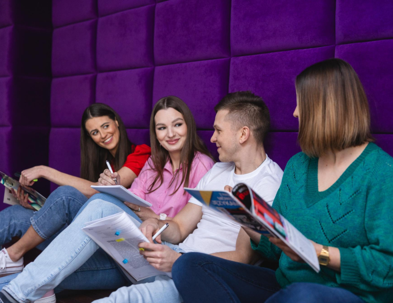 Stypendia i zniżki | Uniwersytet WSB Merito w Toruniu: Grupa studentów siedzi z książkami na fioletowym tle