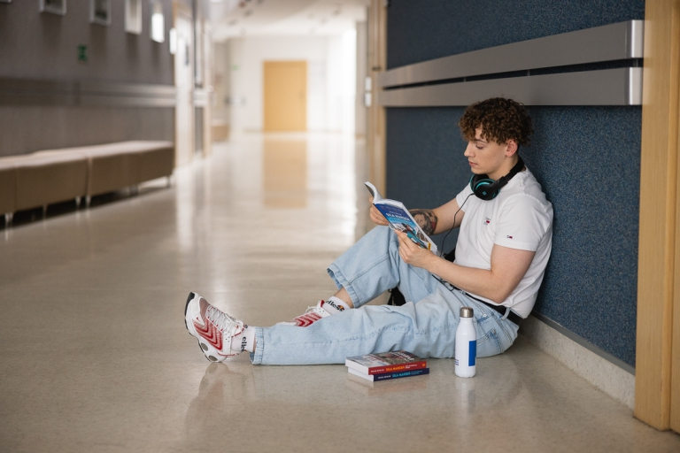 Strefa studenta | Uniwersytet WSB Merito w Toruniu: Główna grafika: Toruń - studia I stopnia - student siedzący na korytarzu