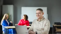 Projektowanie gier komputerowych | Studia podyplomowe w Warszawie | Uniwersytet WSB Merito Warszawa: uśmiechnięty mężczyzna siedzący przed laptopem