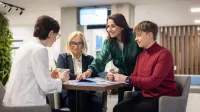 Polityka wynagrodzeń i wartościowanie stanowisk w świetle nowych regulacji UE | Studia podyplomowe w Warszawie | Uniwersytet WSB Merito Warszawa: Ludzie przy stole rozmawiają o studiach.