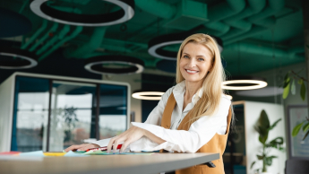 Agile – zwinne metodyki zarządzania projektami | Studia podyplomowe w Warszawie | Uniwersytet WSB Merito Warszawa: uśmiechnięta kobieta przy stole