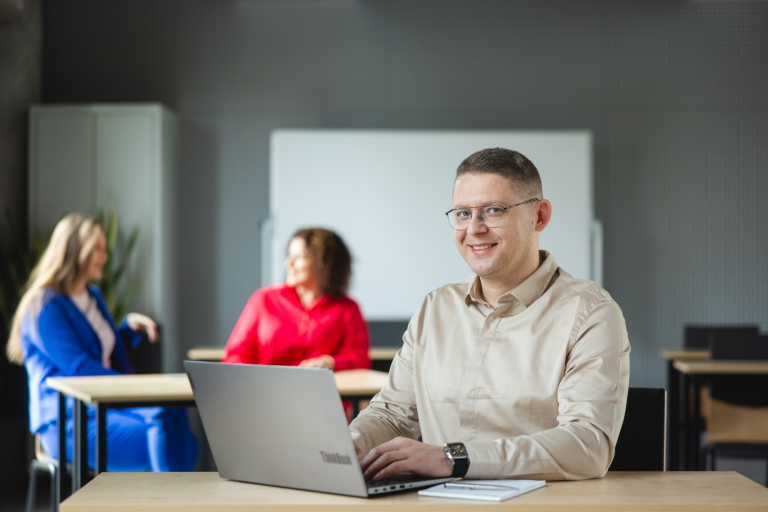 Programowanie aplikacji Java | Studia podyplomowe w Warszawie | Uniwersytet WSB Merito Warszawa: uśmiechnięty mężczyzna siedzący przed laptopem