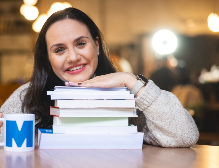 Dietetyka kliniczna | Studia I stopnia we Wrocławiu | Uniwersytet WSB Merito we Wrocławiu: studentka opierająca się o stertę książek i trzymająca kubek w ręce