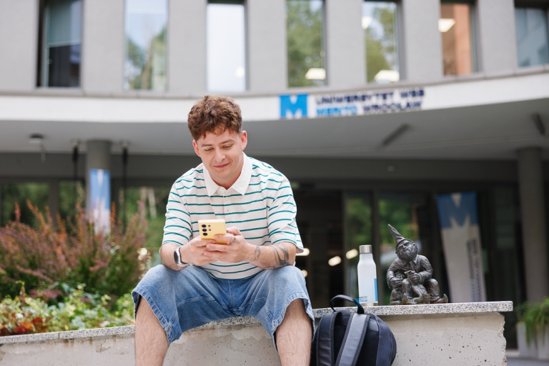 Nasz kampus | Uniwersytet WSB Merito we Wrocławiu: student siedzący obok krasnala przed budynkiem kampusu