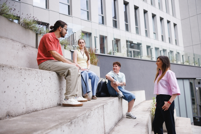 Maturzyści | Uniwersytet WSB Merito we Wrocławiu: Grafika główna: sekcja poświęcona maturzystom - czwórka studentów siedzi na schodach przy budynku uczelni i rozmawiają